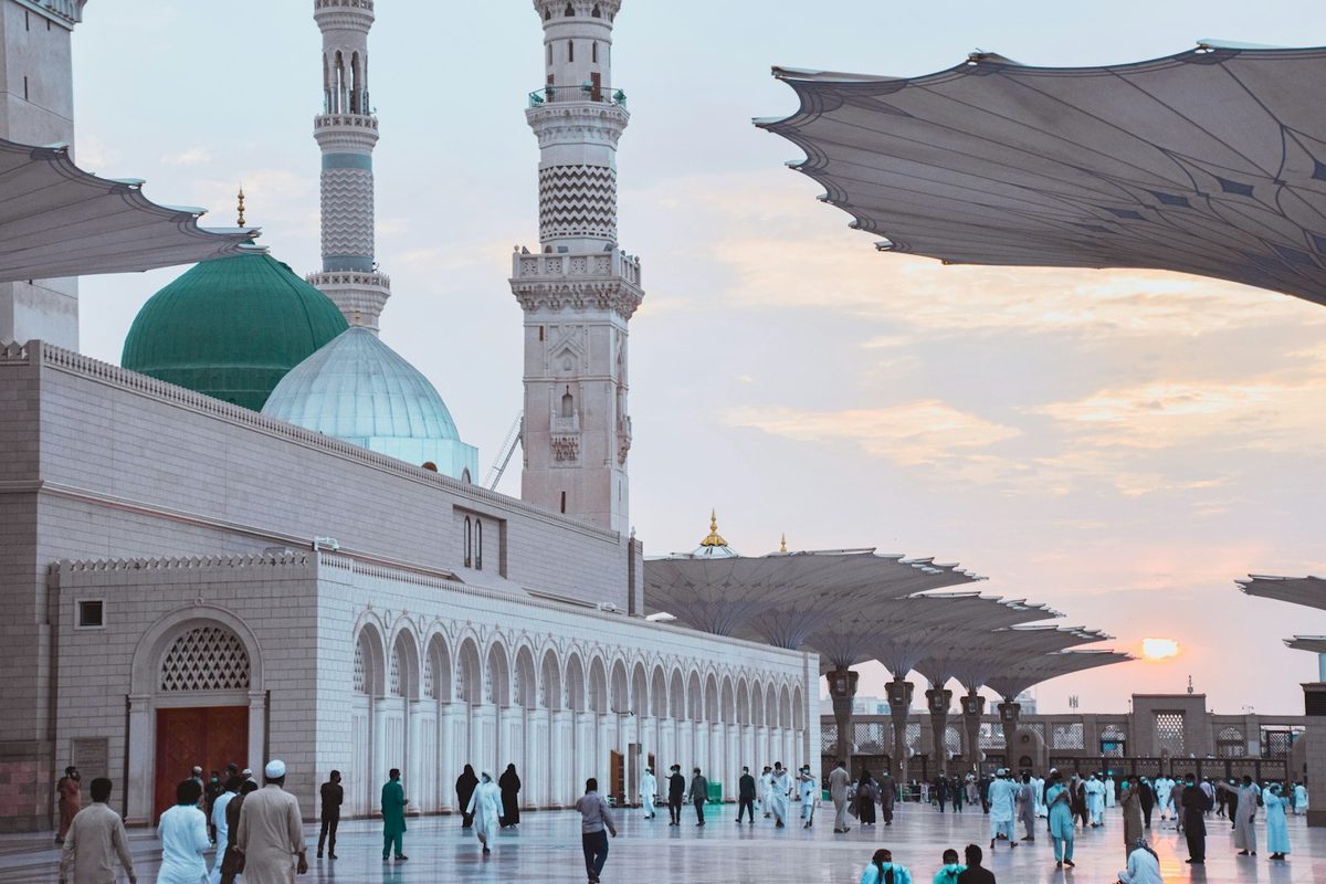 Masjid an-Nabawi in Madinah at sunset, with pilgrims crossing the courtyard
